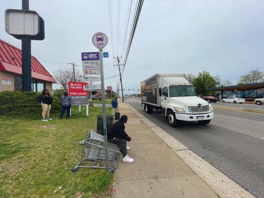 Man sitting on a shopping cart due to there being no basic transit infrastructure at a bus stop.