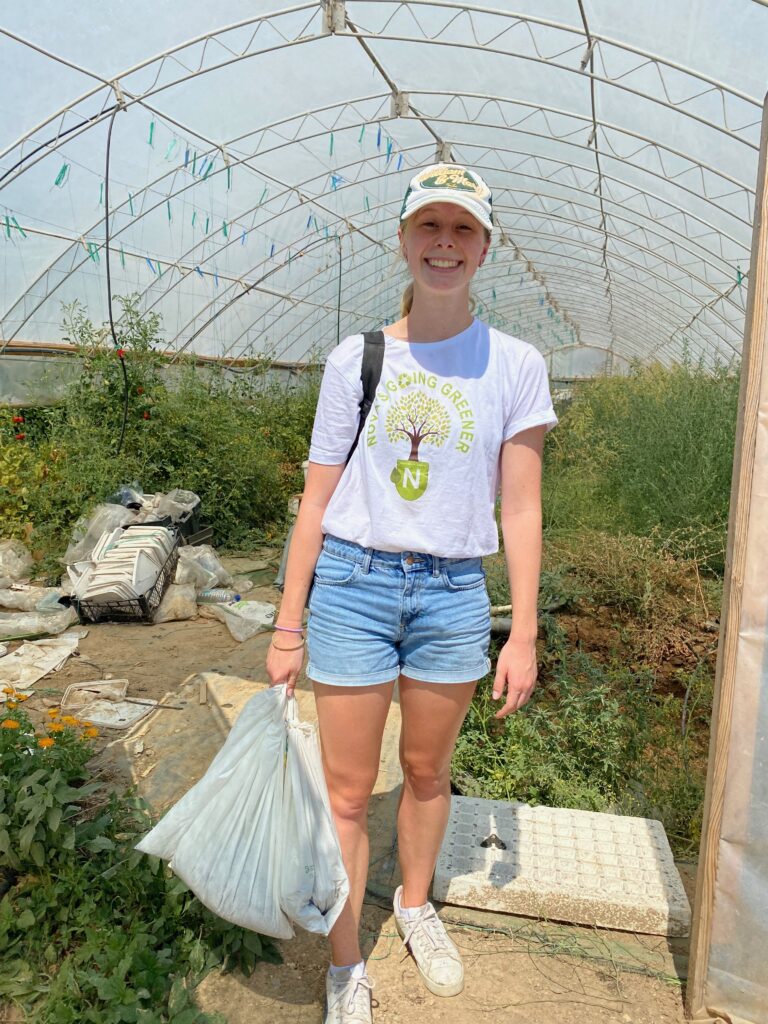 Caroline standing outside a greenhouse with bags of dirt in her hand