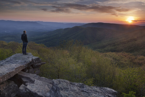 Man standing on the edge of a cliff watching the sunset.