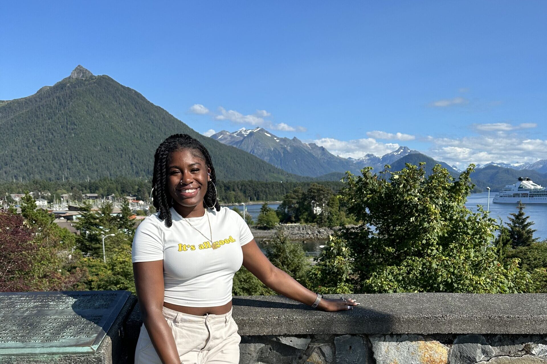 Anjel Iriaghomo in Sitka, Alaska posing at monument with mountains in the background